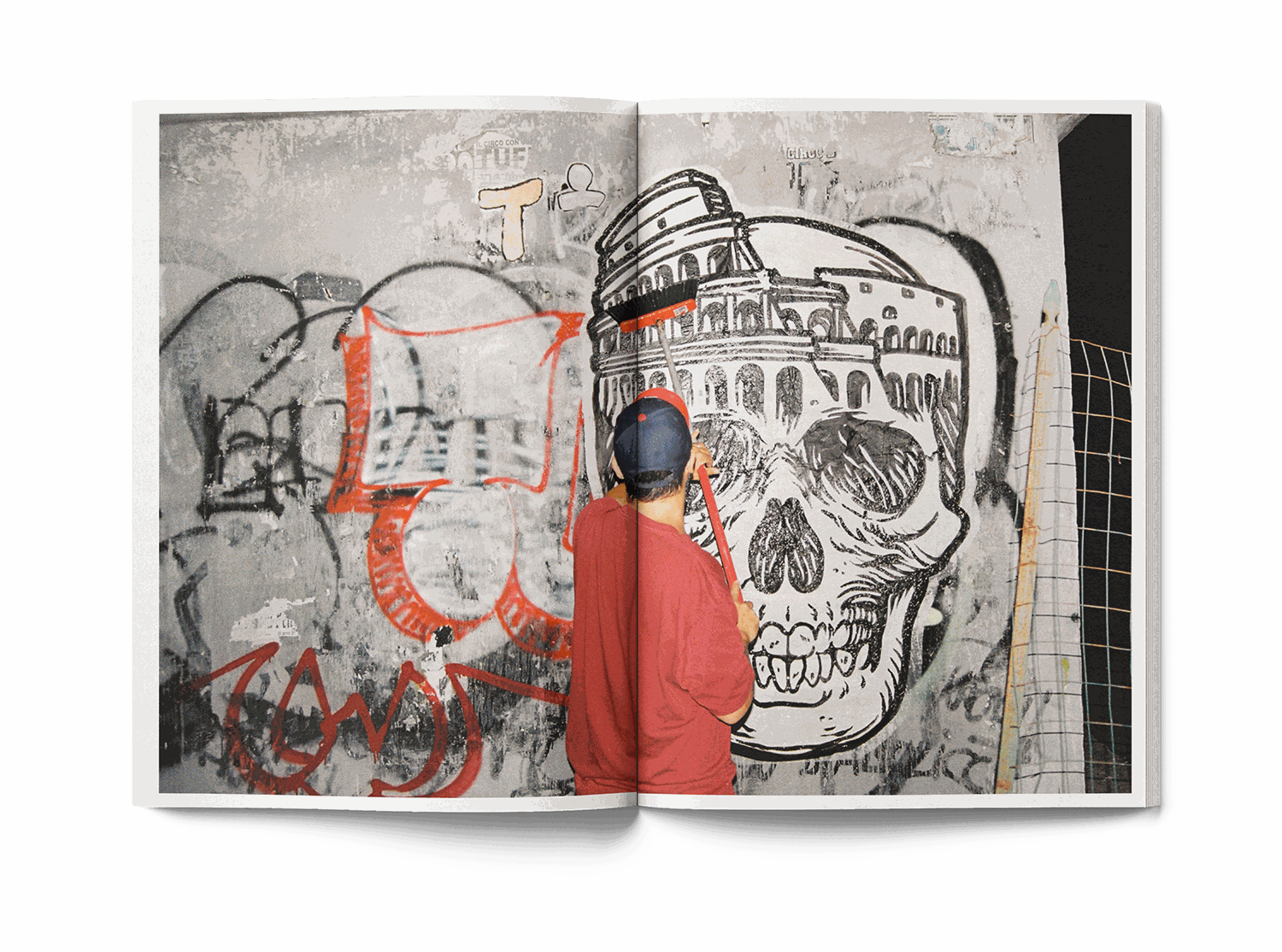 Open book showing street art mural with skull and Colosseum, man in red shirt painting wall, Lucamaleonte Colla 00139 book photo