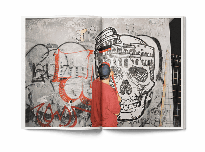 Open book showing street art mural with skull and Colosseum, man in red shirt painting wall, Lucamaleonte Colla 00139 book photo