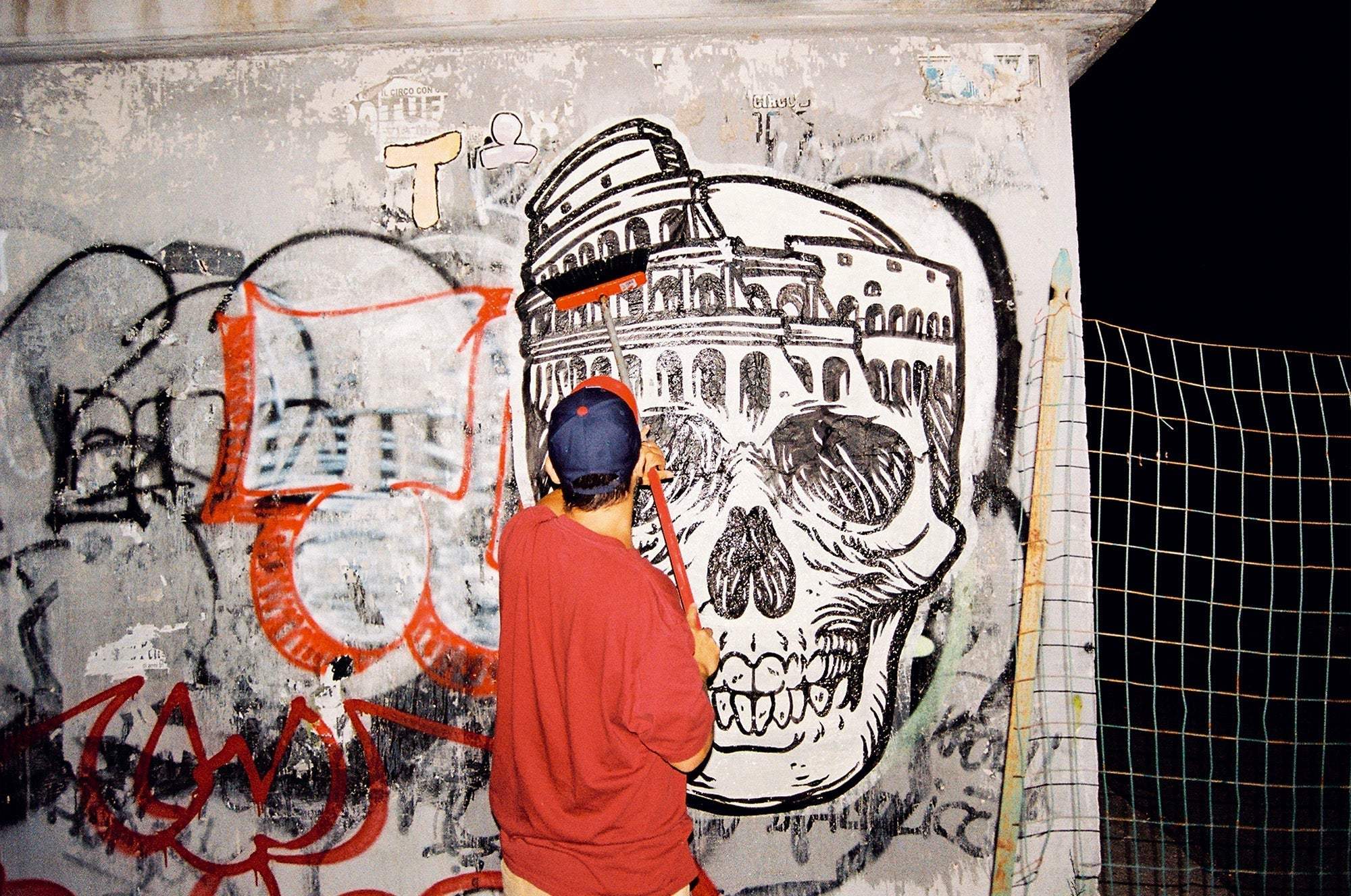 Artist painting large street art mural of skull with Colosseum by Lucamaleonte Colla 00139