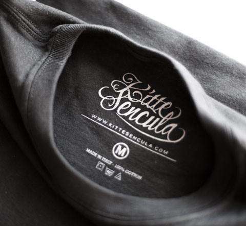 Close-up of black Kittesencula Mescal Tee collar and label showing fabric and size details