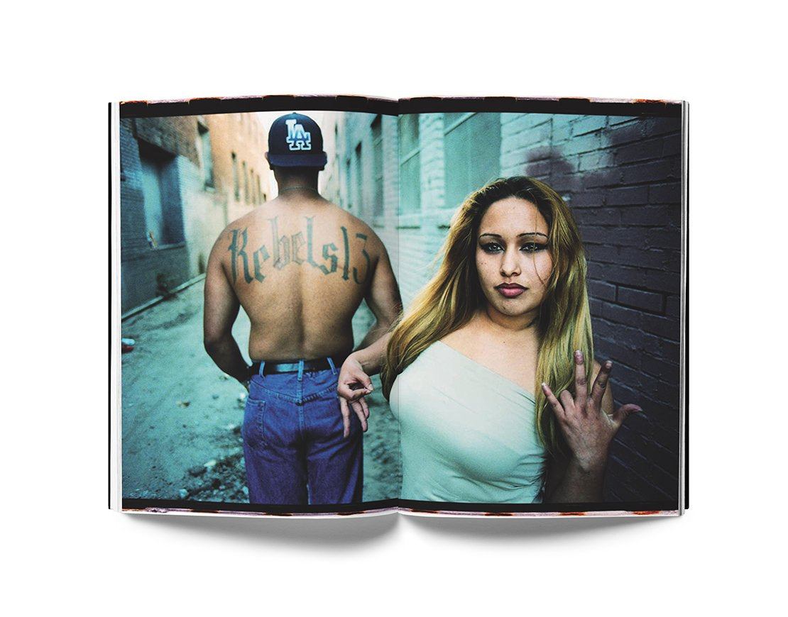 Open book showing LA gang culture portraits by Estevan Oriol with a tattooed man and a woman in an urban alley
