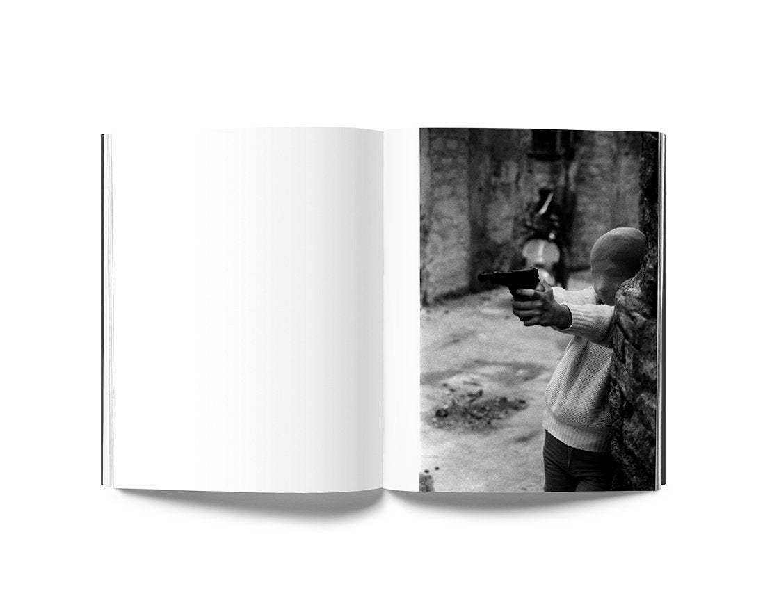 Open book showing a black and white photo of a child holding a gun on a street, from Letizia Battaglia Anthology photography book.