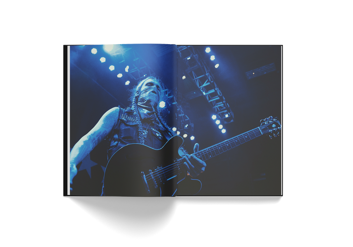 Open book showing a full-page photo of Yelawolf playing guitar on stage under blue lights from Edward Crowe's Yelawolf 51/50 hardcover book.