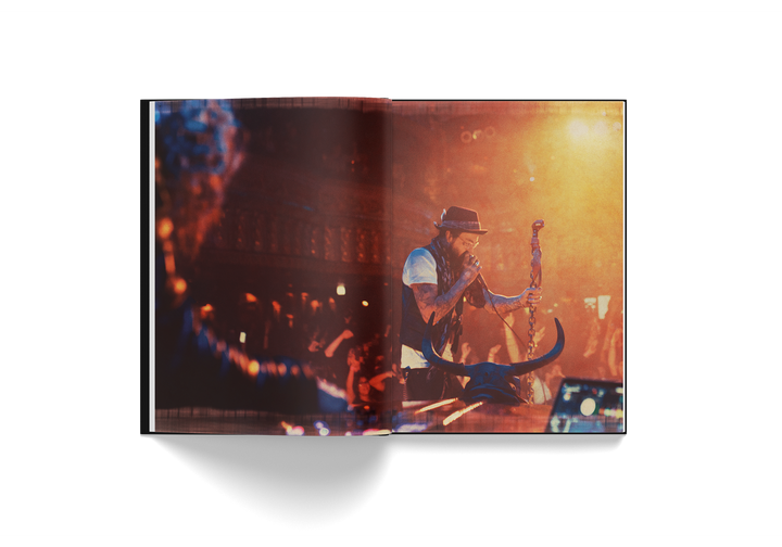 Open hardcover book "Yelawolf 51/50" featuring live concert photo of rapper Yelawolf on stage with microphone and bull skull prop in warm lighting